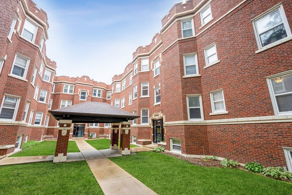 Front view of a red brick apartment building with multiple windows and a central walkway.