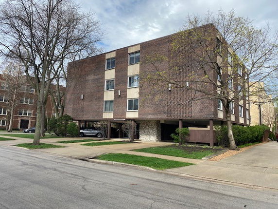 Front view of a multi-story brick apartment building with open parking underneath.