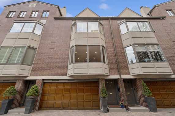 Front view of a multi-story brick townhouse with large windows and wooden garage doors.
