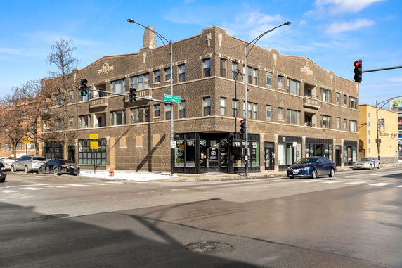 Front view of a multi-story brick building on a street corner with shops and windows.