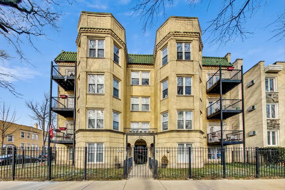 Front view of a multi-story brick apartment building with balconies and a gated entrance.