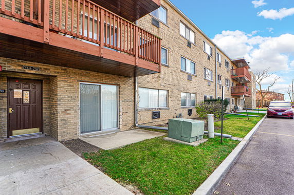 Front view of a multi-story brick apartment building with balconies and parking area.