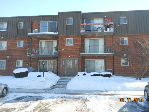 Front view of a three-story brick apartment building with balconies and snow on the ground.