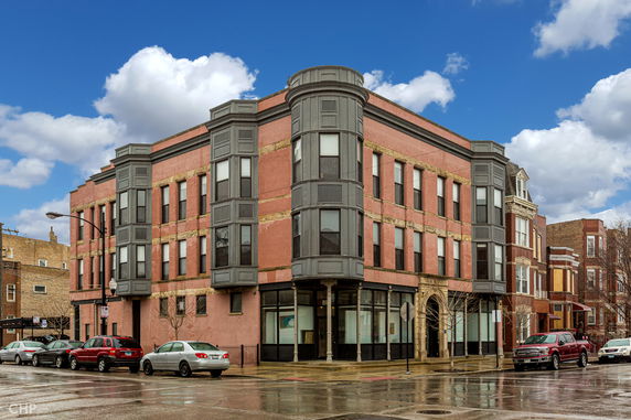 Front view of a three-story brick building with large windows on a corner lot.