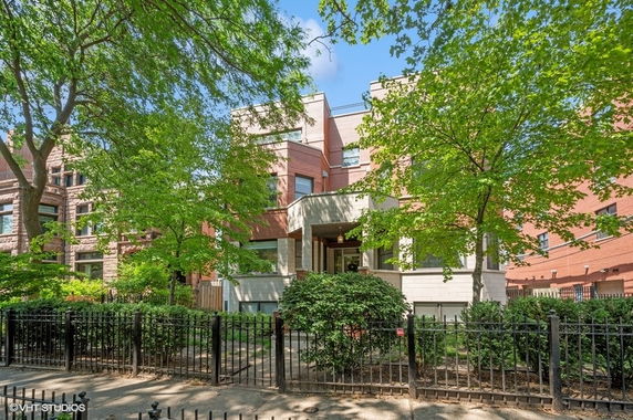 Front view of a multi-story brick building with trees and a fence in the foreground.