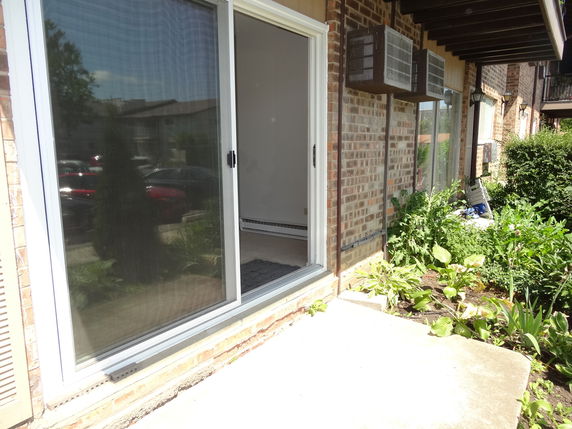 Side view of a brick building with sliding glass doors and air conditioning units.
