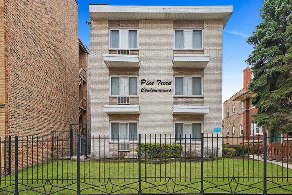 Front view of a multi-story condominium building with a fenced lawn.