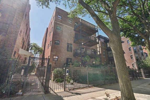 Front view of a multi-story brick building with balconies and a gated entrance.