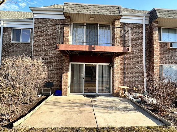Front view of a two-story brick house with balcony and sliding glass doors.