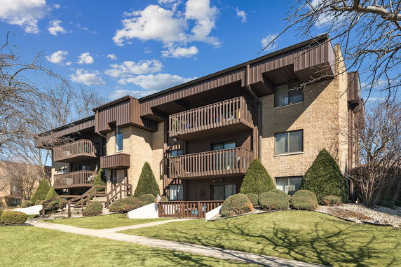 Front view of a multi-story residential building with balconies and landscaped surroundings.