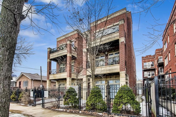 Front view of a multi-story brick building with balconies and a fenced entrance.