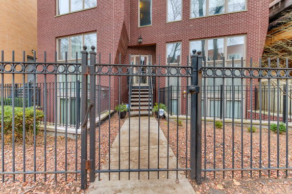 Front view of a multi-story brick house with large windows and a gated entrance.