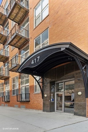 Front view of a multi-story brick building with metal balconies and a large entrance canopy.