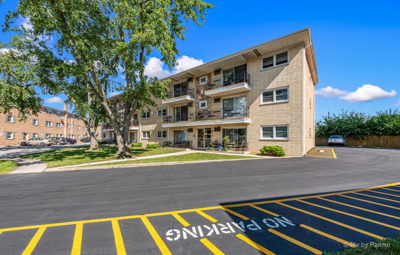 Front view of a three-story residential building with balconies and a parking area.