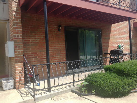 Front view of a building with a brick exterior, metal railings, and a patio area with a grill.