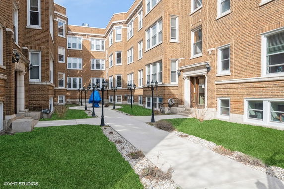 Front view of a multi-story brick building with a sidewalk and grassy courtyard.
