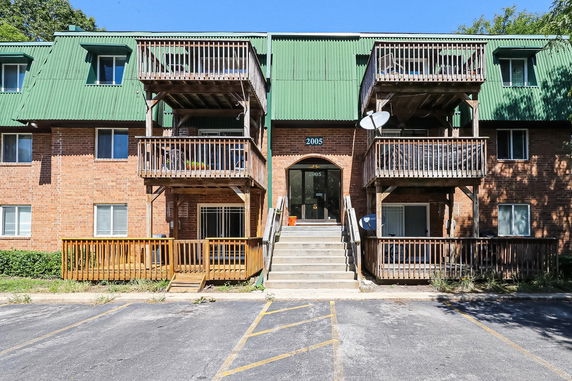 Front view of a multi-story brick apartment building with green roof and balconies.