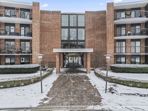 Front view of a brick residential building with balconies and glass entrance.