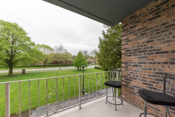 View from a balcony with metal railing overlooking a grassy lawn and trees.