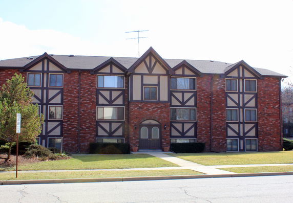 Front view of a brick three-story apartment building with tudor-style accents.