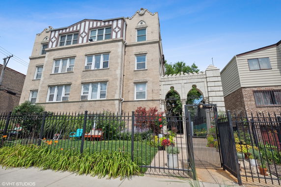Front view of a multi-story brick apartment building with decorative features and a gated entrance.