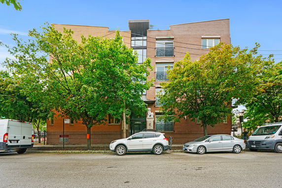 Front view of a multi-story brick building with trees along the street.