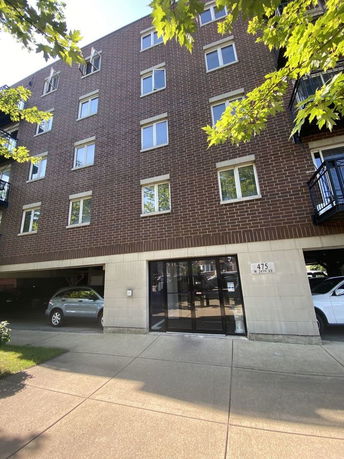 Front view of a multi-story brick apartment building with parking area on the ground level.