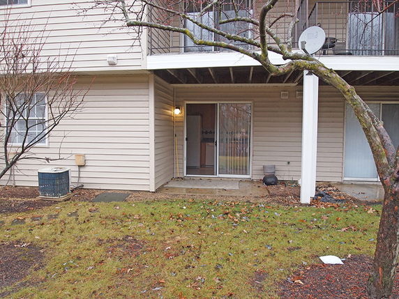 Front view of a two-story residential building with a patio and sliding glass doors on the ground floor.