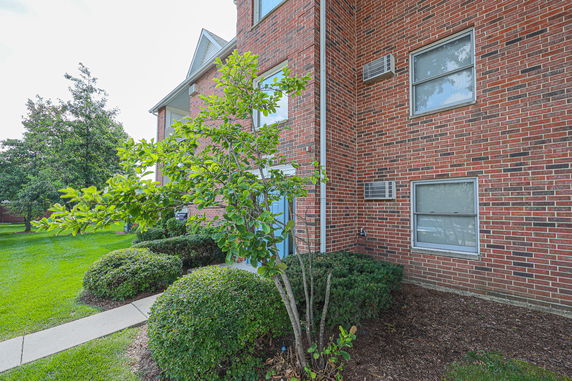 View of a brick exterior of a multi-story building with windows and air conditioning units.