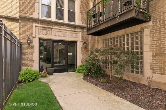 Front view of a brick building entrance with glass doors and a small balcony.