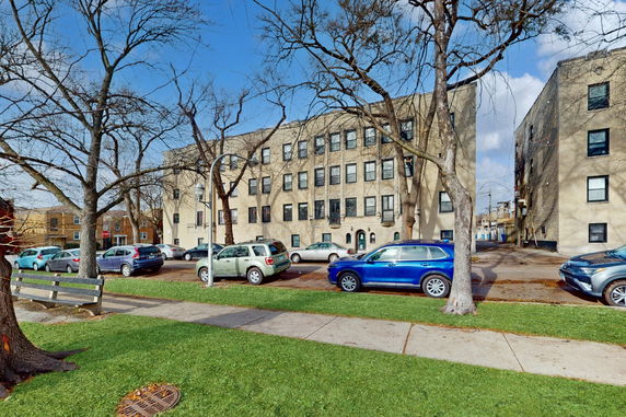 Front view of a multi-story building with several windows and parked cars in front.