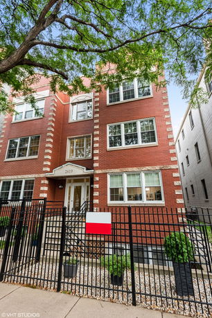 Front view of a multi-story brick building with multiple windows and a gated entrance.