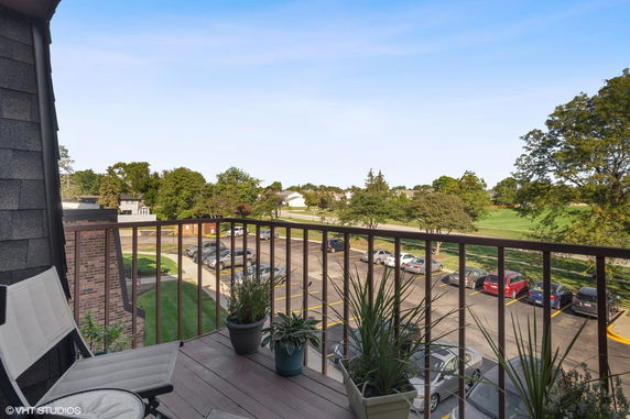 View from a balcony overlooking a parking lot and green landscape.