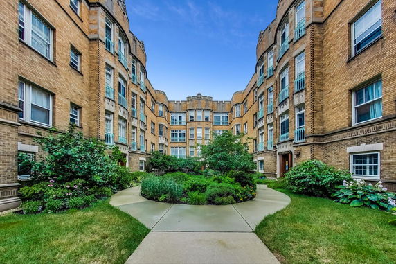 Front view of a multi-story brick building with decorative balconies and a central garden courtyard.
