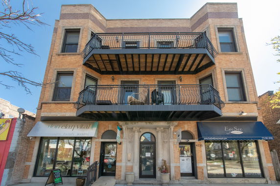 Front view of a three-story brick building with balconies and commercial stores on the ground floor.