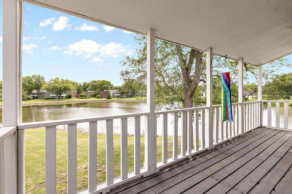 Balcony view overlooking a lake and trees with houses in the distance.