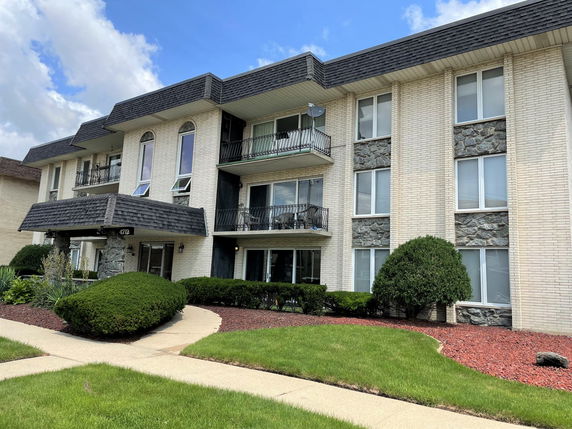 Front view of a multi-story residential building with balconies and a landscaped entrance.