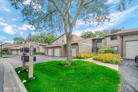 Front view of a row of attached townhouses with garages and garden areas.