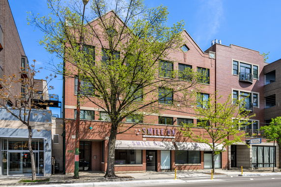 Front view of a multi-story brick building with commercial establishments on the ground floor.