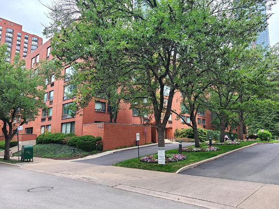 Front view of a multi-story brick apartment building with trees and landscaping.