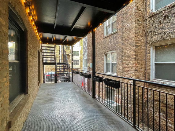 A walkway with metal railings and stairway outside a brick building.