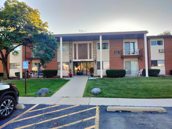 Front view of a two-story building with balconies and a parking area.