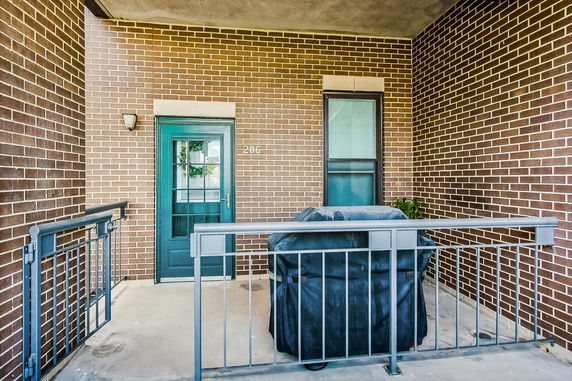 Outdoor view of an apartment entrance with a brick wall and a covered grill on a small patio.