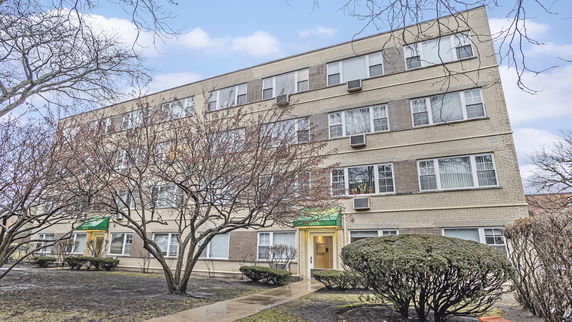 Front view of a multi-story apartment building with multiple windows and green awnings.