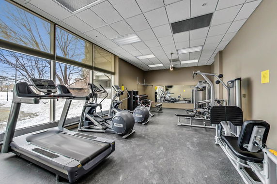 Exercise room with various gym equipment and large windows.