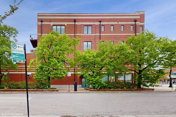 Front view of a three-story brick building with large windows and surrounding trees.