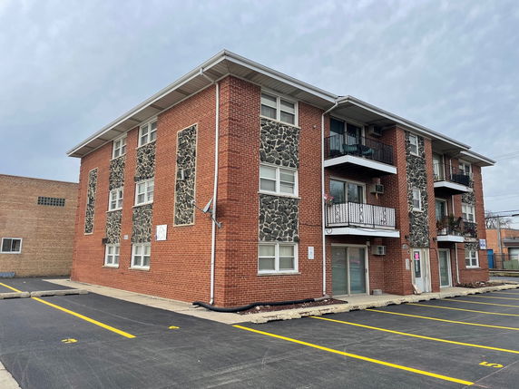 Front view of a three-story brick apartment building with stone accents and balconies.