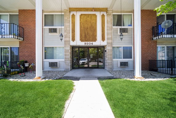 Front view of a multi-story residential building with brick and stone facade, displaying large columns and a glass entrance door.