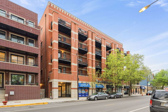 Front view of a multi-story brick building with balconies and shops on the ground floor.