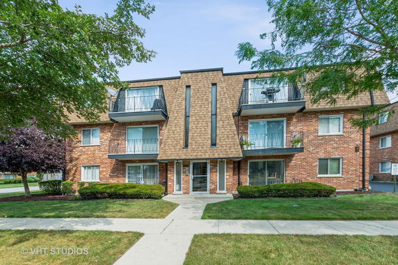 Front view of a multi-story brick apartment building with balconies.